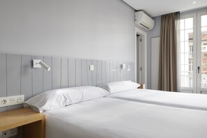 Two single beds with white linens, a nightstand, and a city view.