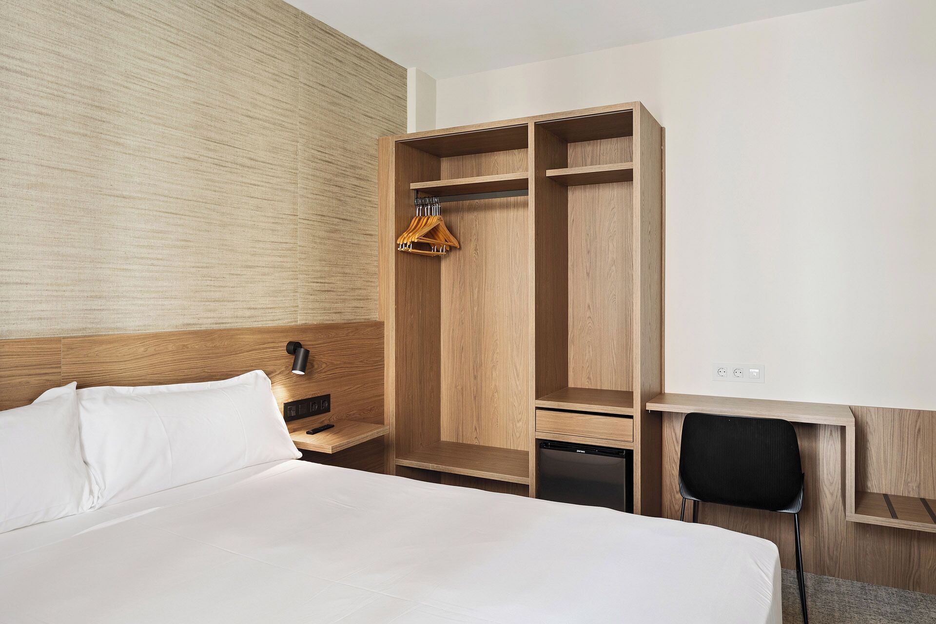 Una habitación de hotel con una cama grande, un armario de madera, un escritorio con una silla y un pequeño electrodoméstico negro.