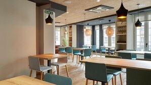 A modern restaurant with wooden tables and teal chairs, large windows, and hanging pendant lights. - Hotel Avenida (Pamplona)