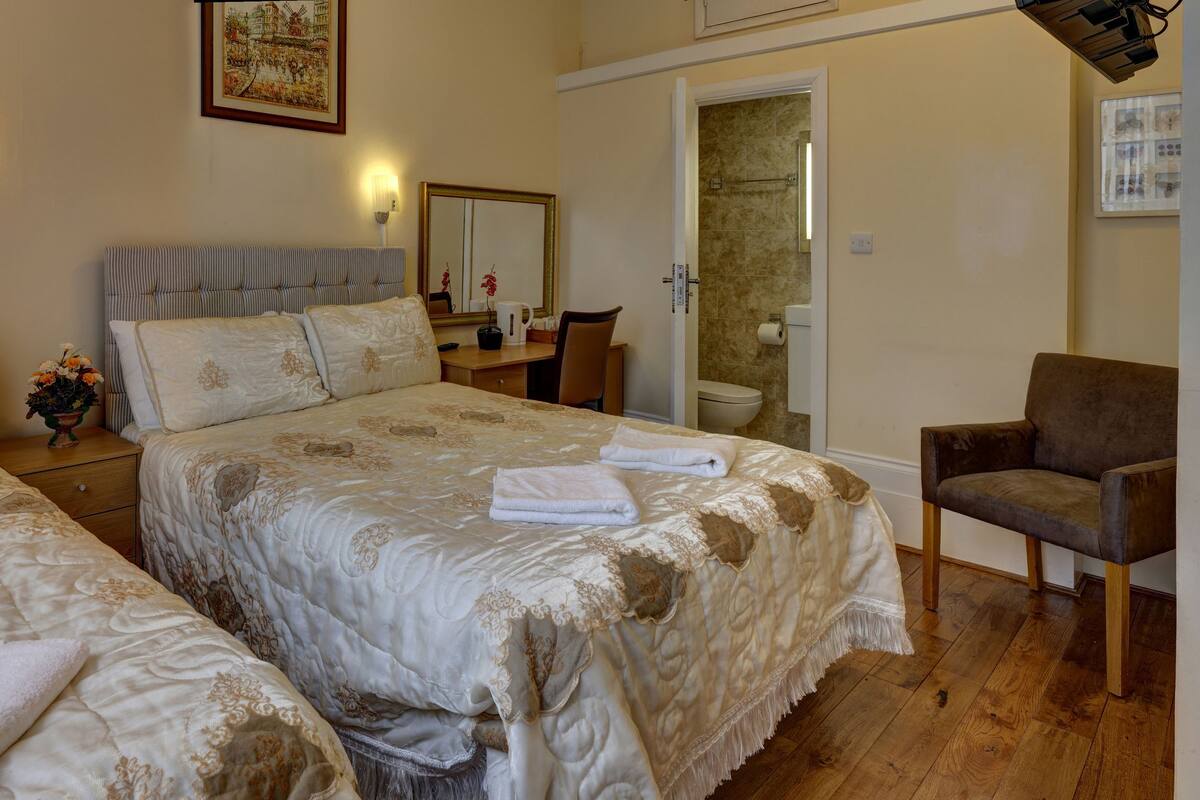 A hotel room with two beds, a desk, a chair, a bathroom, and a shower.