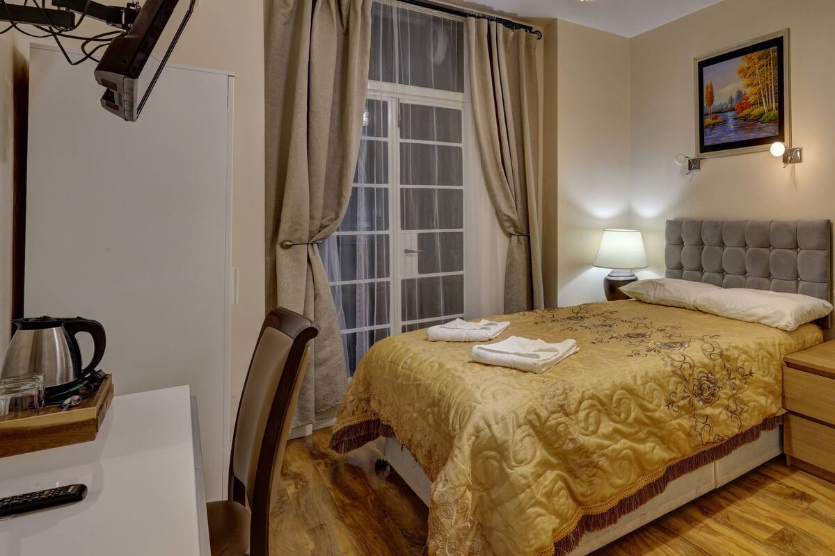 A hotel room with a bed, bedside table, lamp, and a painting on the wall.