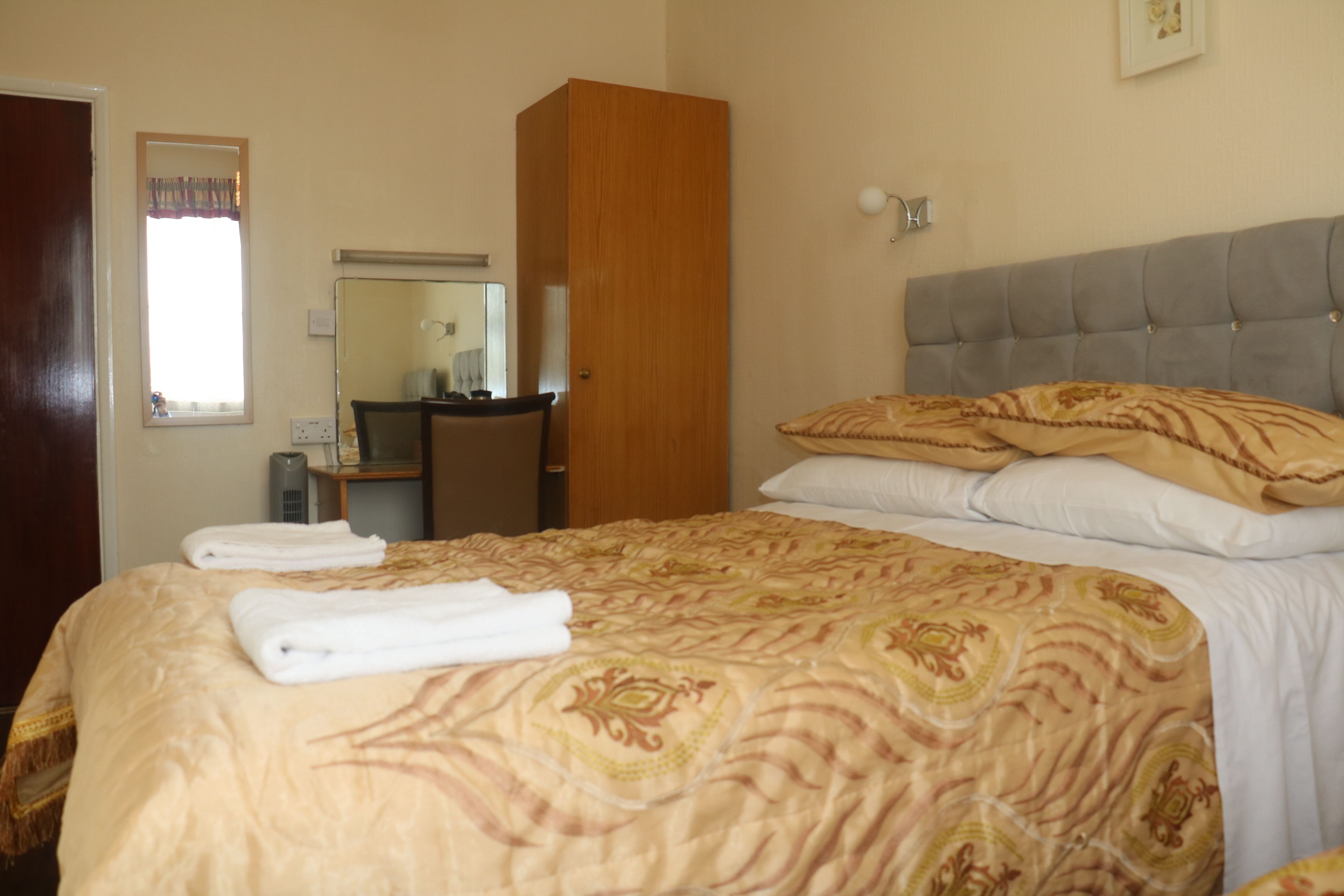 A hotel room with a bed, a wardrobe, a desk, and a mirror.