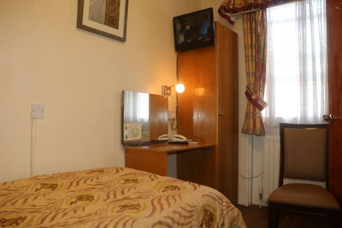A hotel room with a bed, a desk with a telephone, a mirror, a chair, and a window with curtains.