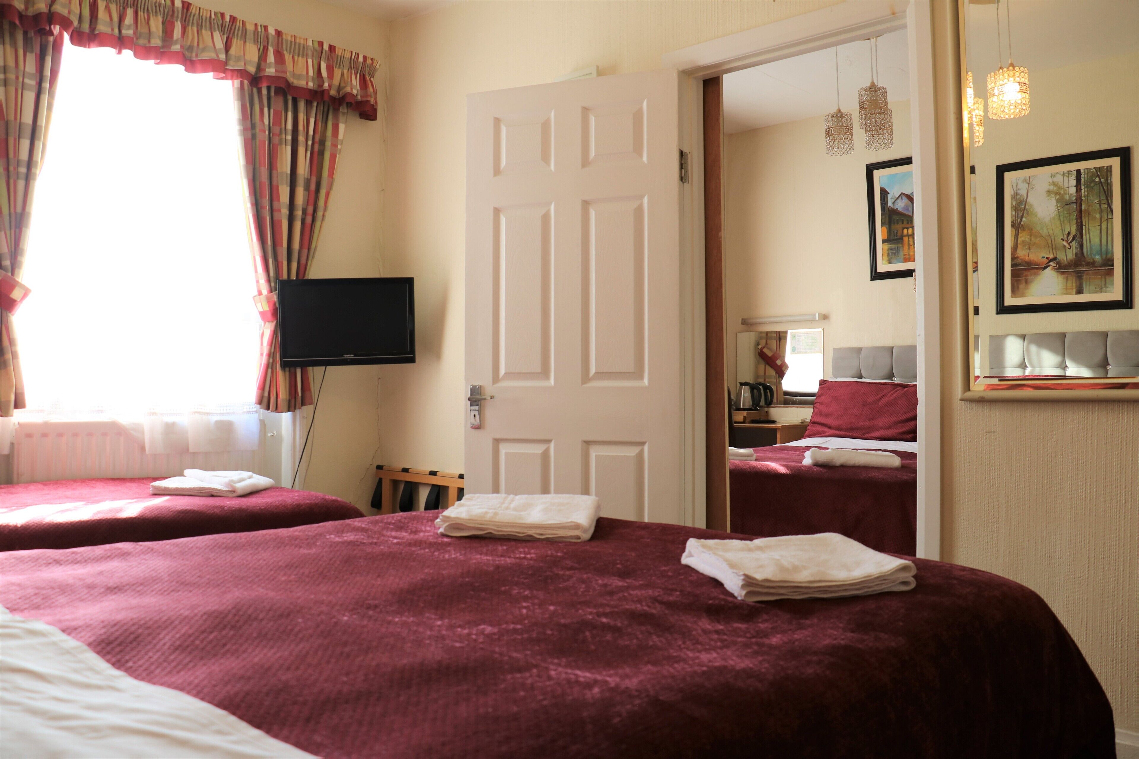 A hotel room with two beds, a television, a door leading to another room, and artwork on the wall.