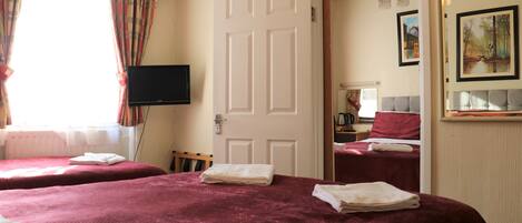 A hotel room with two beds, a television, a door leading to another room, and artwork on the wall.