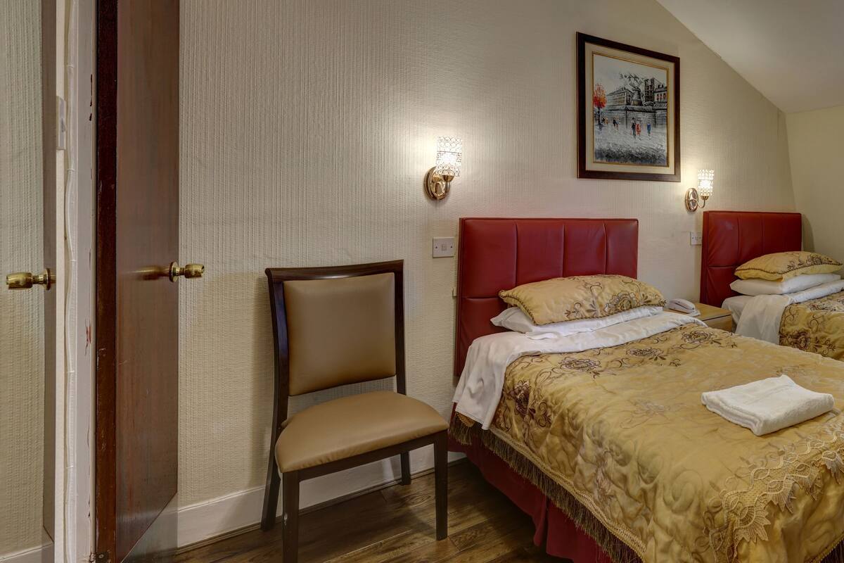 A hotel room with two beds, a desk, a chair, a radiator, and a window with curtains.