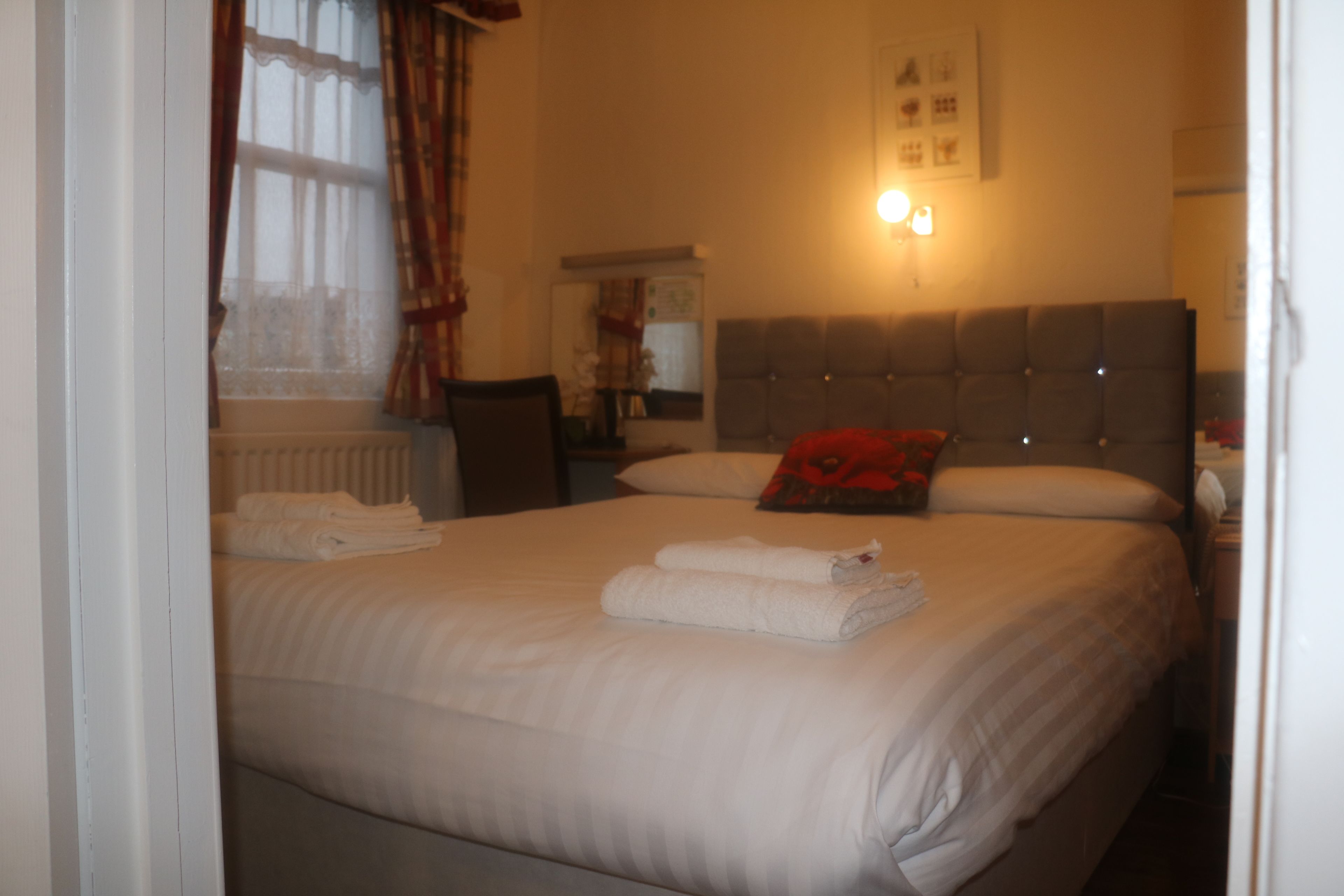 Una habitación de hotel con cama, mesita de noche, lámpara y ventana con cortinas.