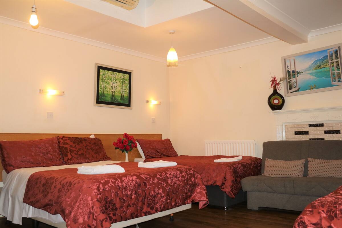 A hotel room with two beds, a sofa, a painting, and a vase with flowers.