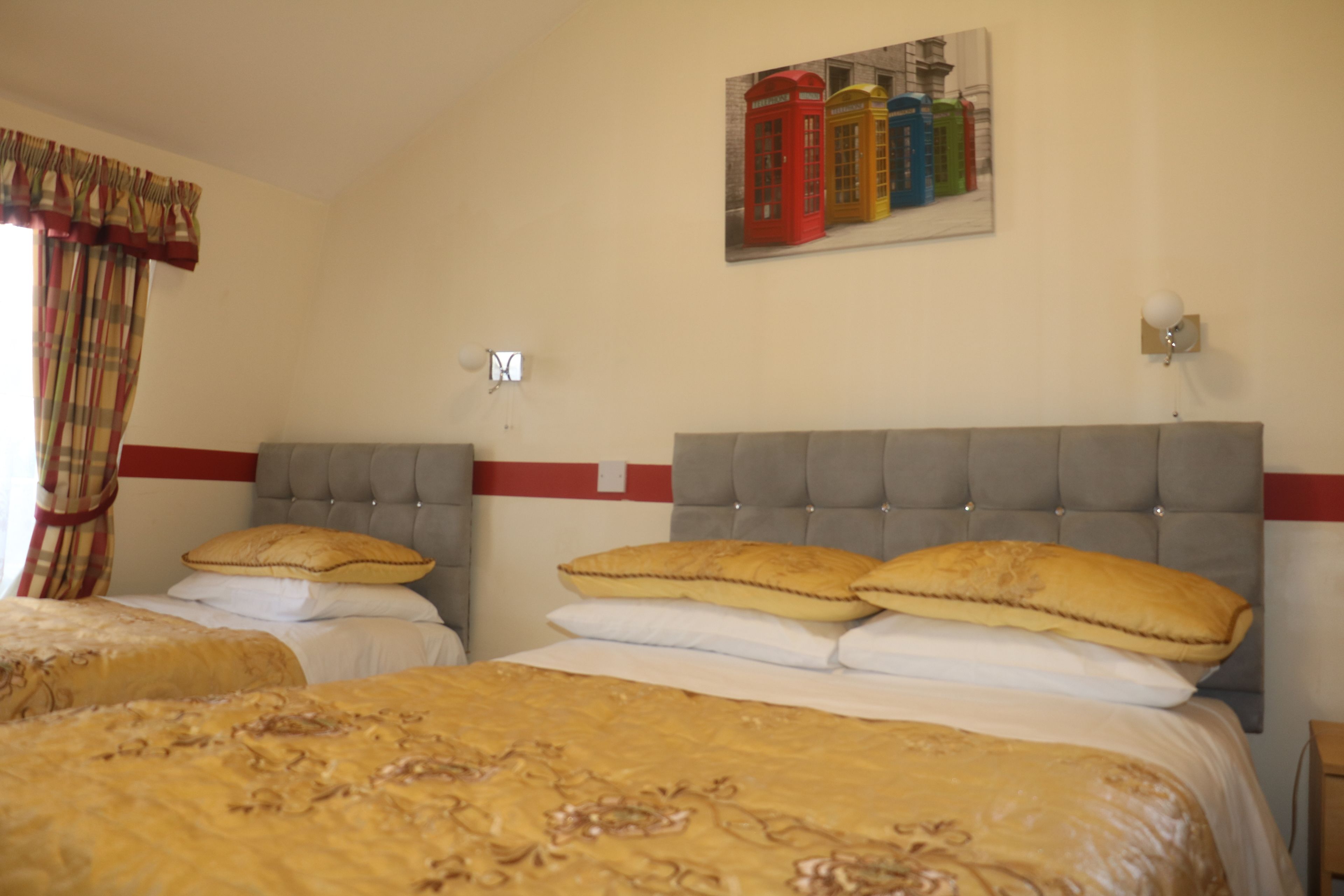 A hotel room with two beds, a red and white striped wall, a painting of red, yellow, and blue telephone booths, and a light switch on the wall.
