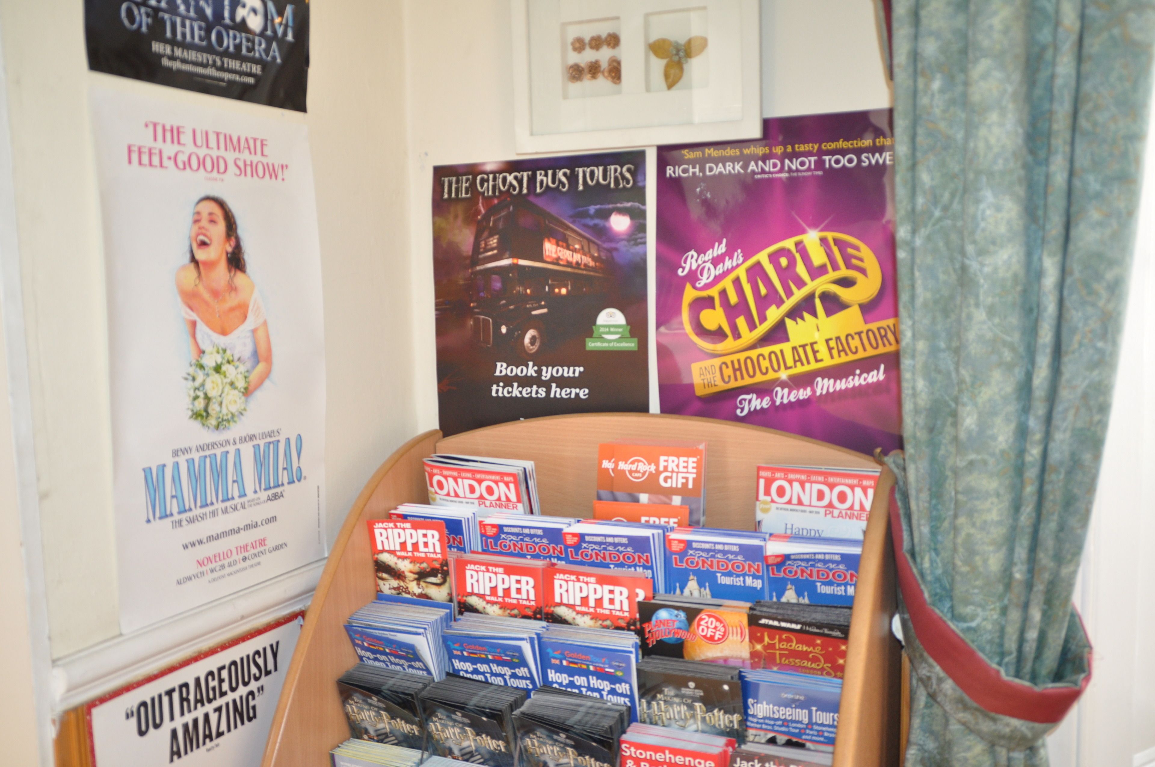 A display of London tourist maps and tickets for shows like 'The Ghost Bus Tours' and 'Charlie and the Chocolate Factory'.