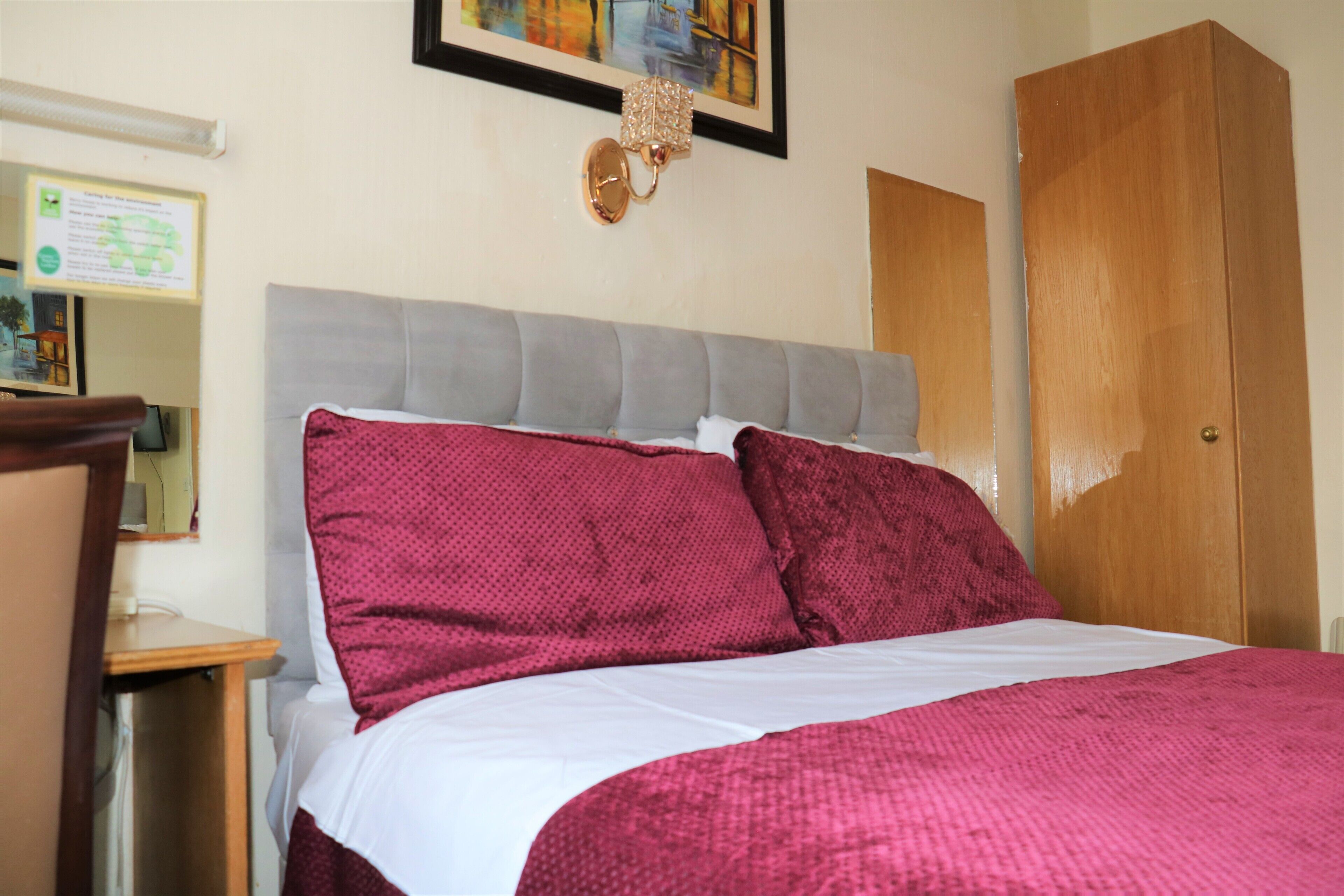 A bedroom with a bed, a nightstand, a wooden wardrobe, and a wall-mounted light fixture.