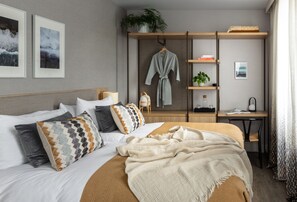 A neatly arranged bedroom with a bed, pillows, a bedside table, a desk, and a robe hanging on a rack. - Inhabit Southwick Street, a Member of Design Hotels (London)