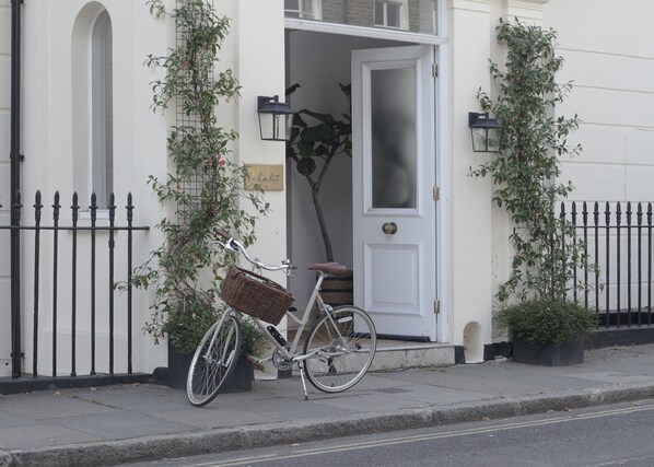 A bicycle with a basket parked in front of a white building with a door and a sign that reads "Lighthouse". - Inhabit Southwick Street, a Member of Design Hotels (London)