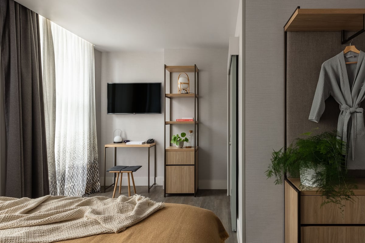 A modern bedroom with a bed, a desk, a TV, and a wardrobe.