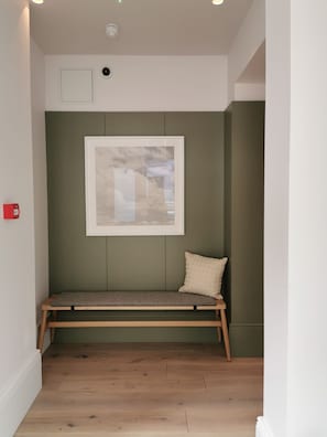 A bench with a cushion against a green wall, a framed picture above, and a ceiling light. - Inhabit Southwick Street, a Member of Design Hotels (London)