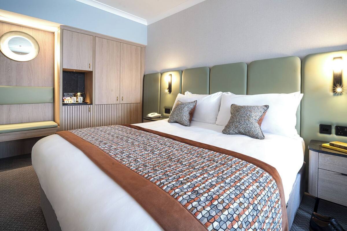 A hotel room with a large bed, a bedside table, a nightstand, a wardrobe, and a built-in shelf.