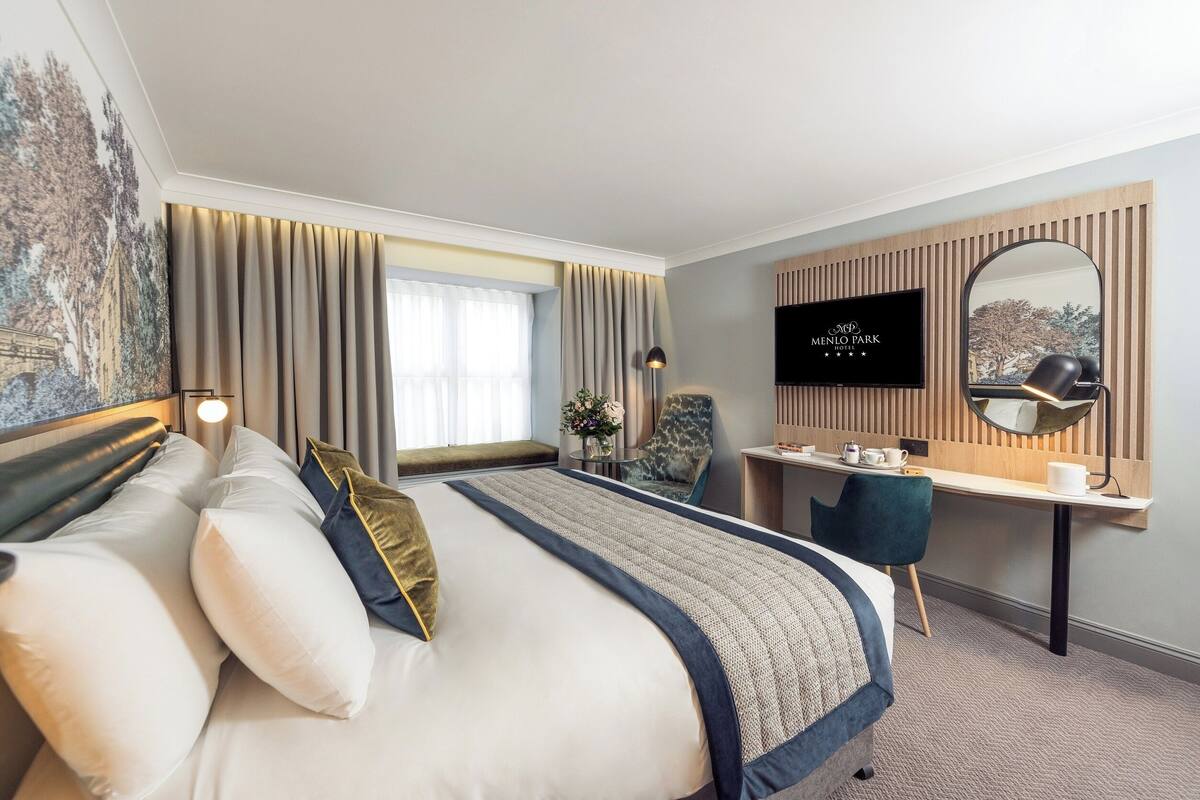 A hotel room with a large bed, a desk, a chair, a TV, and a mirror.