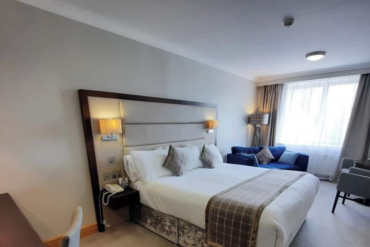 A hotel room with a large bed, bedside lamps, a desk, and a chair.