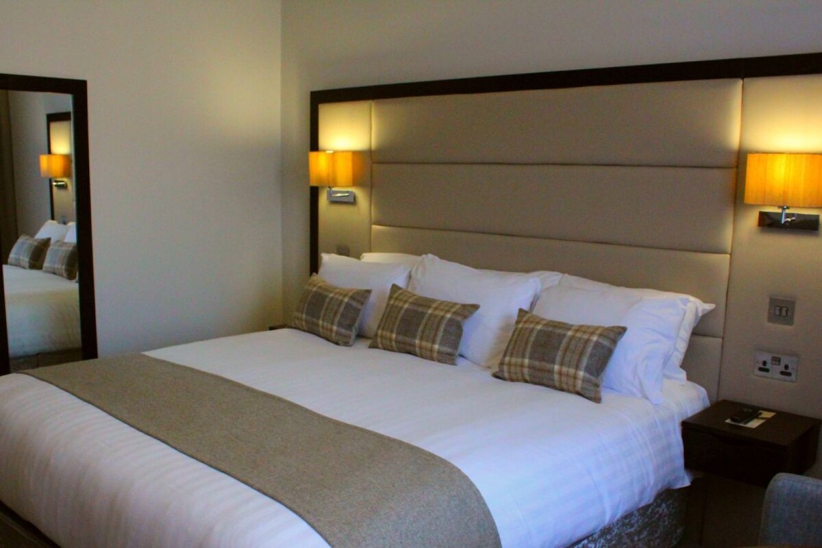A hotel room with a large bed, two bedside lamps, a nightstand, and a mirror.