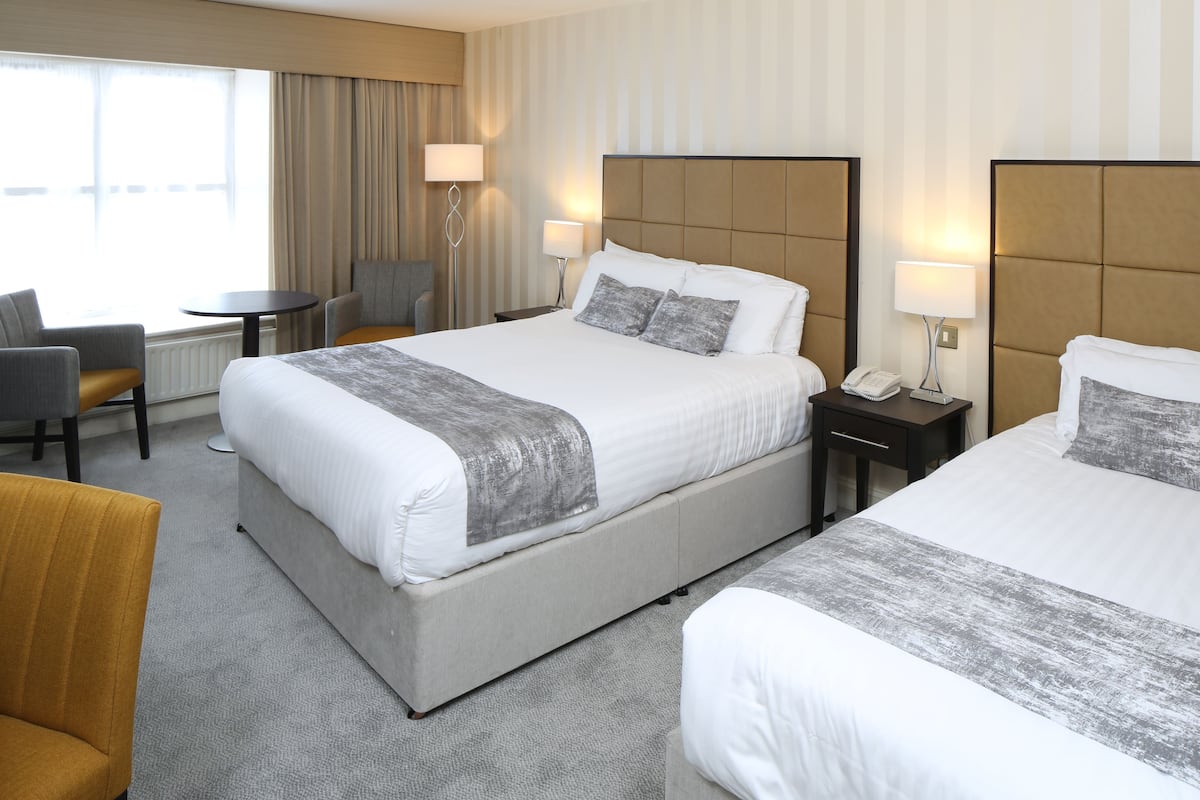 A hotel room with two beds, a desk, a chair, and a window.