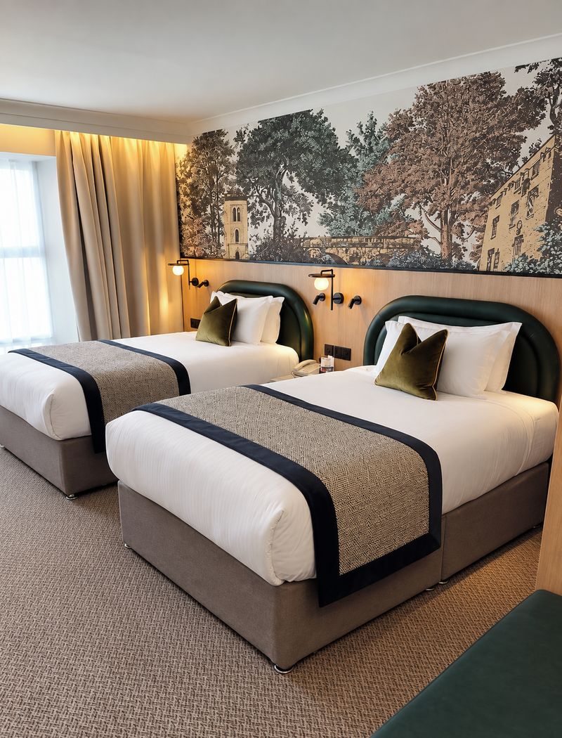 A hotel room with two beds, a large window with curtains, a wall mural, and a carpeted floor.