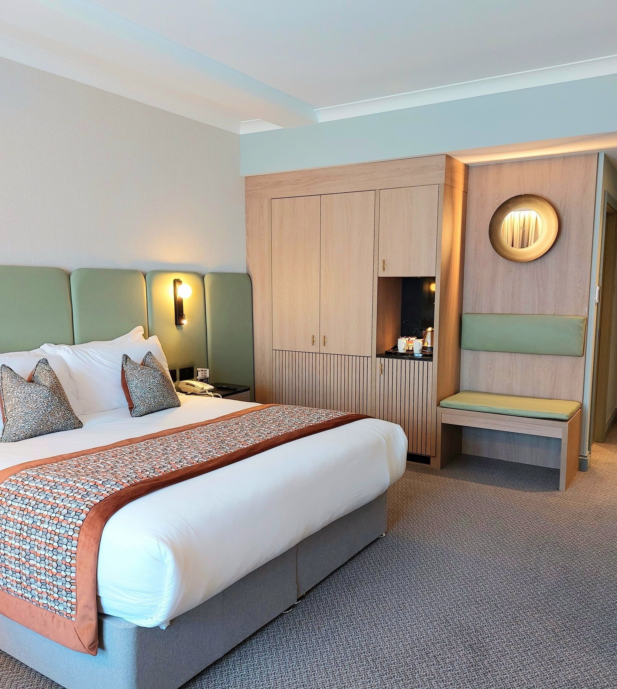 Une chambre d’hôtel avec un grand lit, un bureau avec une lampe, une armoire et un banc.