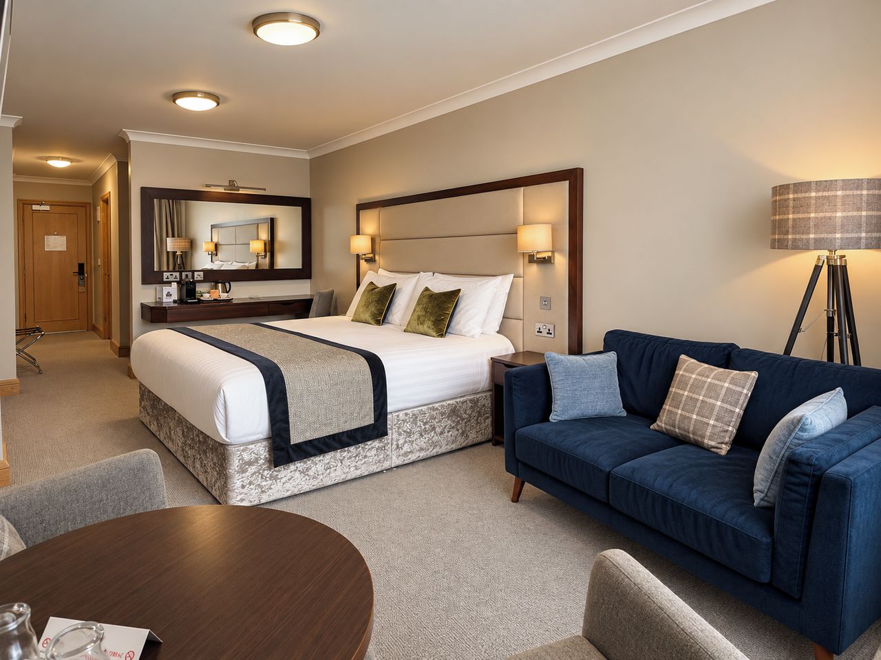 A hotel room with a bed, a sofa, a desk, and a lamp.