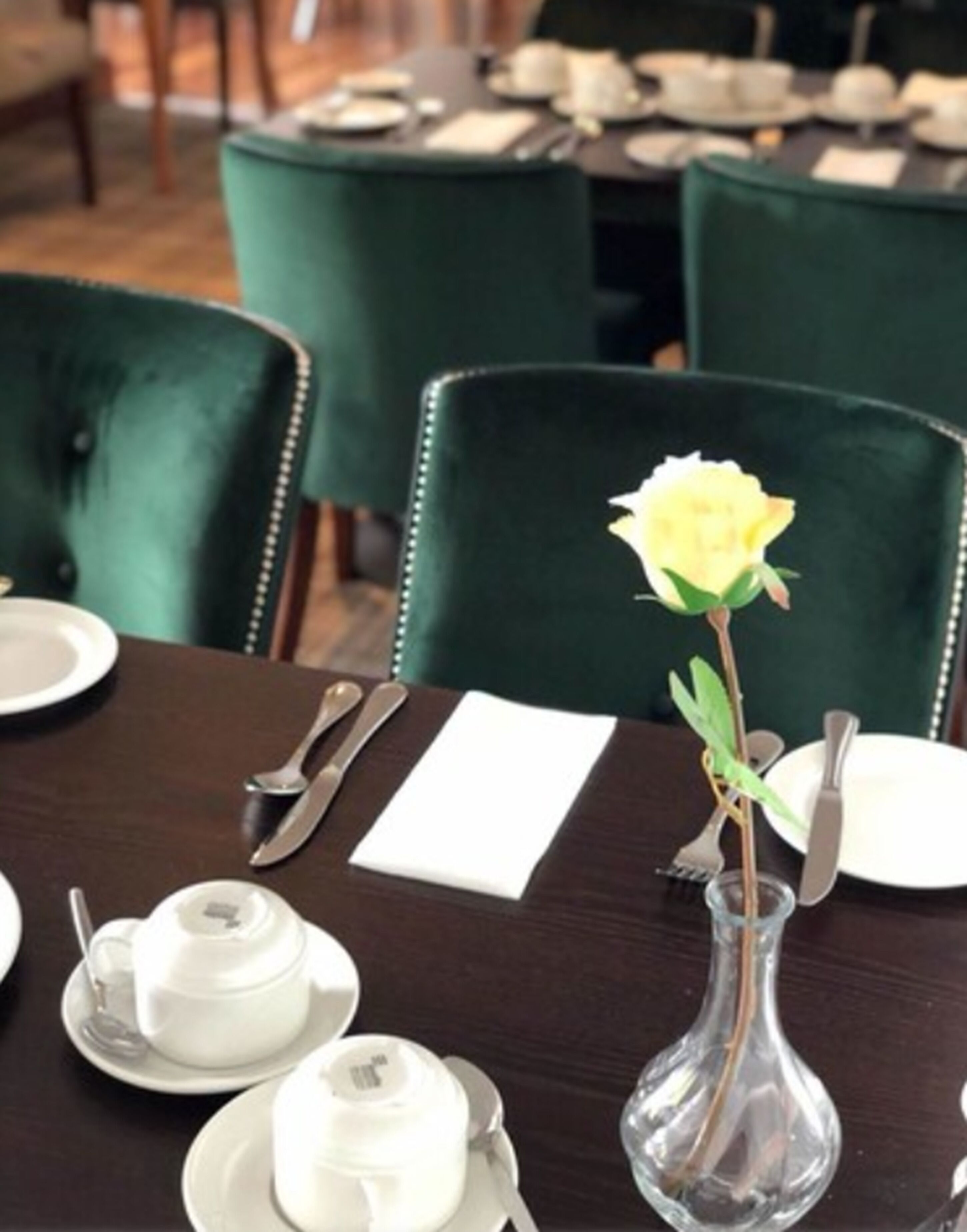 A dining table set with white dishes, silverware, and a clear glass vase with a yellow flower.