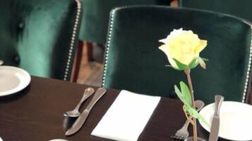 Una mesa de comedor dispuesta con vajilla blanca, cubiertos y un florero de vidrio transparente con una flor amarilla.