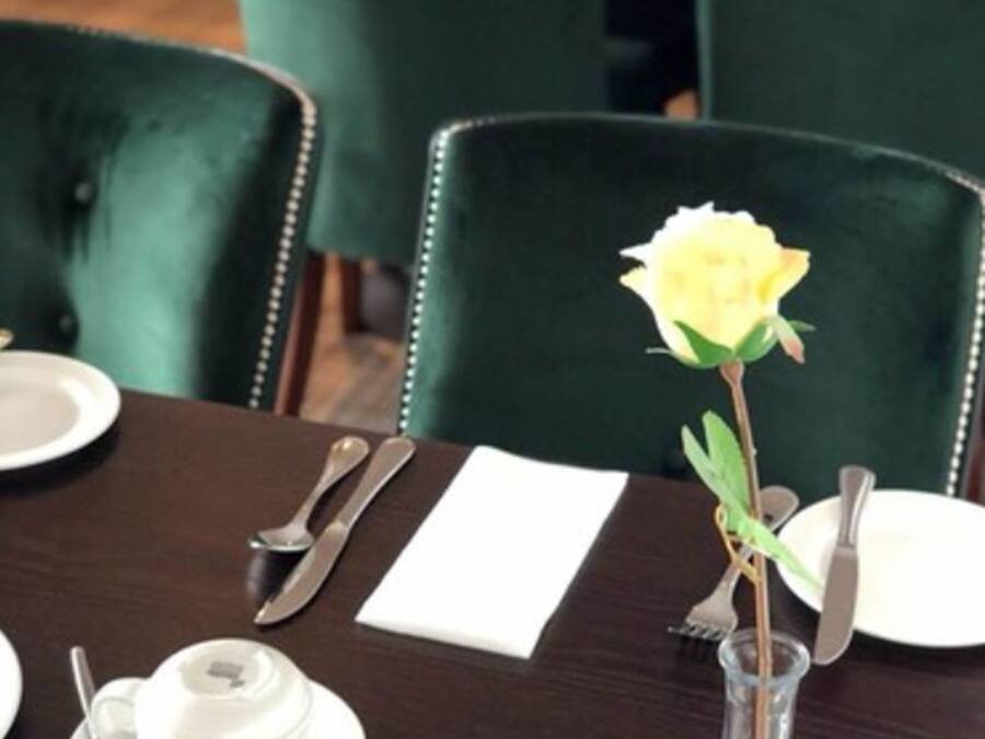 Una mesa de comedor dispuesta con vajilla blanca, cubiertos y un florero de vidrio transparente con una flor amarilla.
