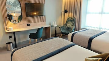 A hotel room with two beds, a desk, a chair, a TV, and a window with curtains.