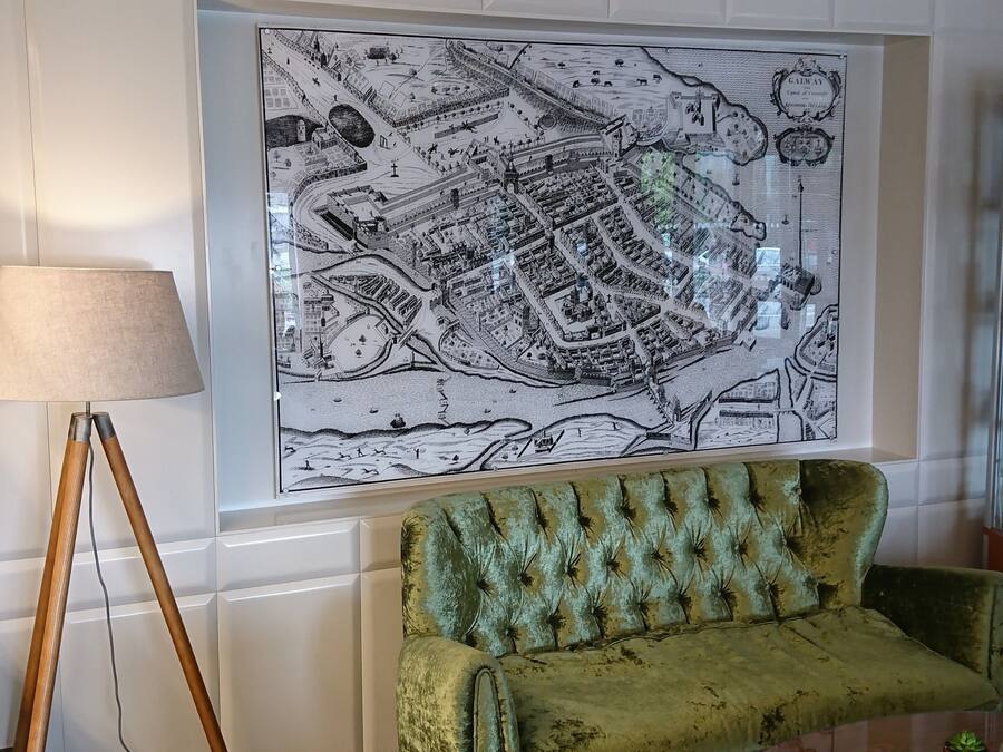 A room with a large black and white map on the wall, a green velvet sofa, a small round table, and a floor lamp.