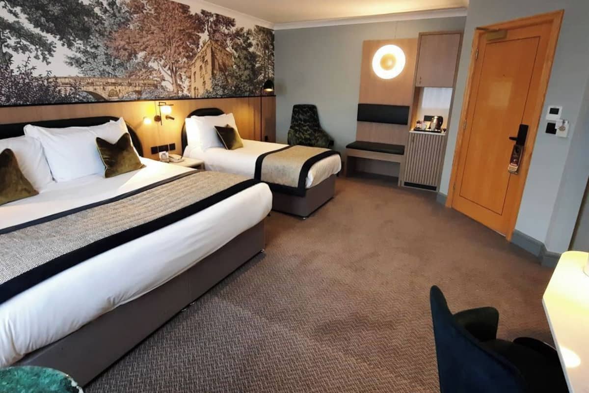 A hotel room with two beds, a mural on the wall, a desk, and a chair.