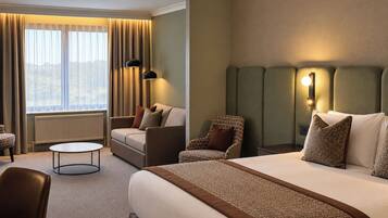 Habitación de hotel con una cama grande, un sofá, una silla, una mesita y vistas al exterior.
