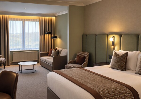 Habitación de hotel con una cama grande, un sofá, una silla, una mesita y vistas al exterior.