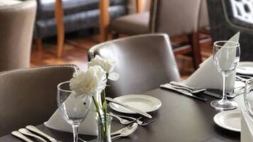 A dining table set with white plates, silverware, and a vase with white flowers.