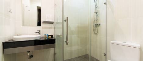 Un baño moderno con ducha envuelta en vidrio, inodoro blanco y lavamanos con espejo superior.