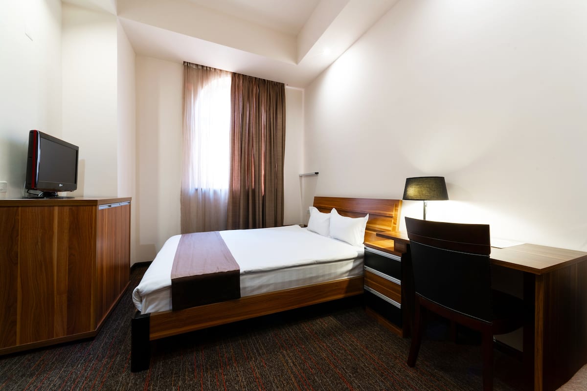 Une chambre d’hôtel équipée d’un lit, d’un bureau, d’une chaise, d’une télévision et de rideaux.