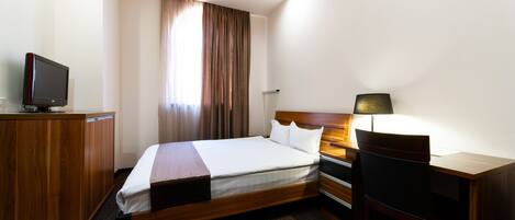 A hotel room with a bed, desk, chair, TV, and curtains.