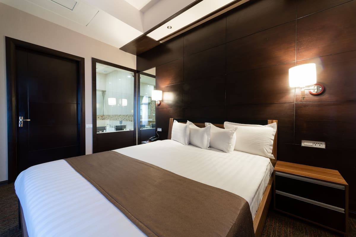 Une chambre d’hôtel avec un grand lit, une table de chevet en bois, un miroir et un luminaire fixé au mur.
