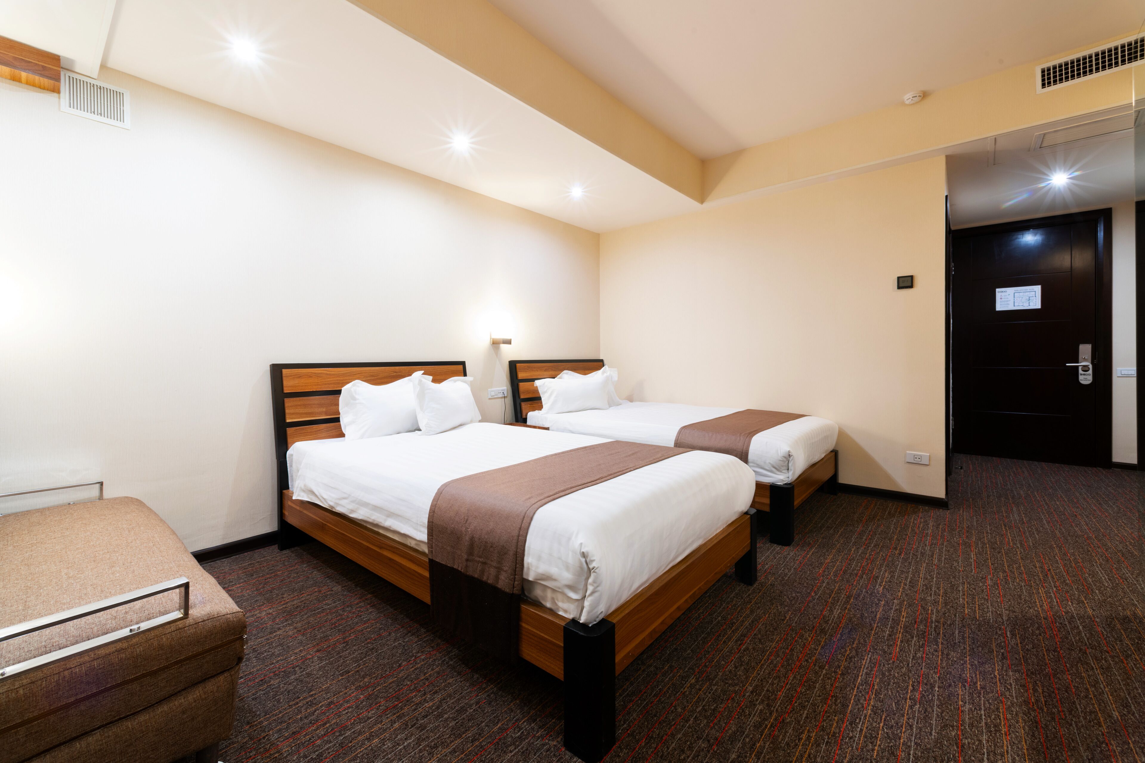 Habitación de hotel con dos camas individuales, cabecera de madera, un escritorio pequeño y piso alfombrado.