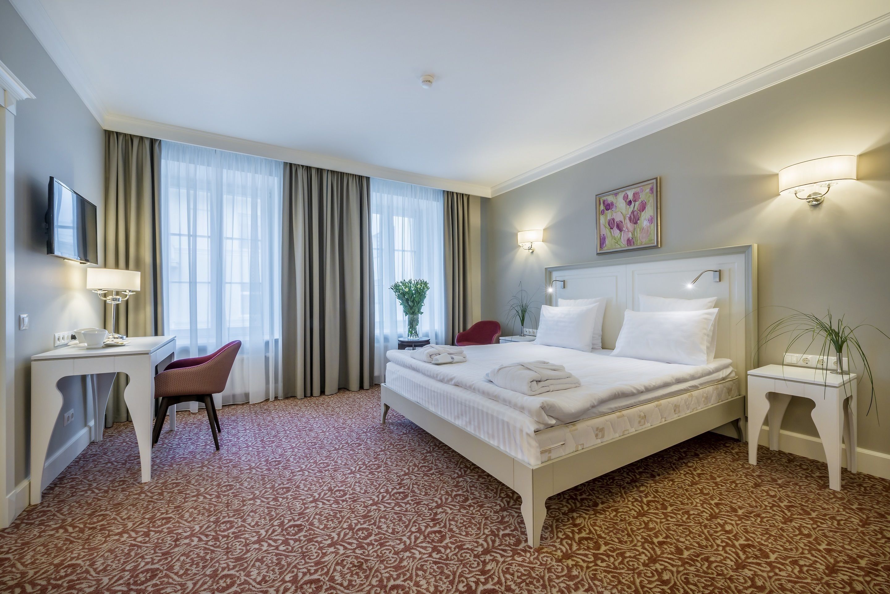 A hotel room with a bed, desk, chair, and a television.