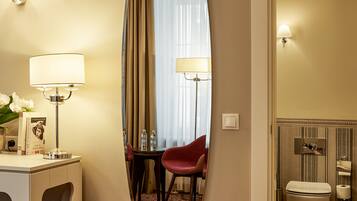 Habitación de hotel con un espejo ovalado grande, un escritorio con lámpara, una silla y una cama con inodoro y bidé.