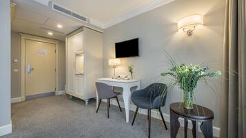 Habitación de hotel con escritorio, dos sillas, televisión, lámpara y planta.