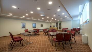 A conference room with multiple tables and chairs, ceiling lights, and framed artwork on the walls.