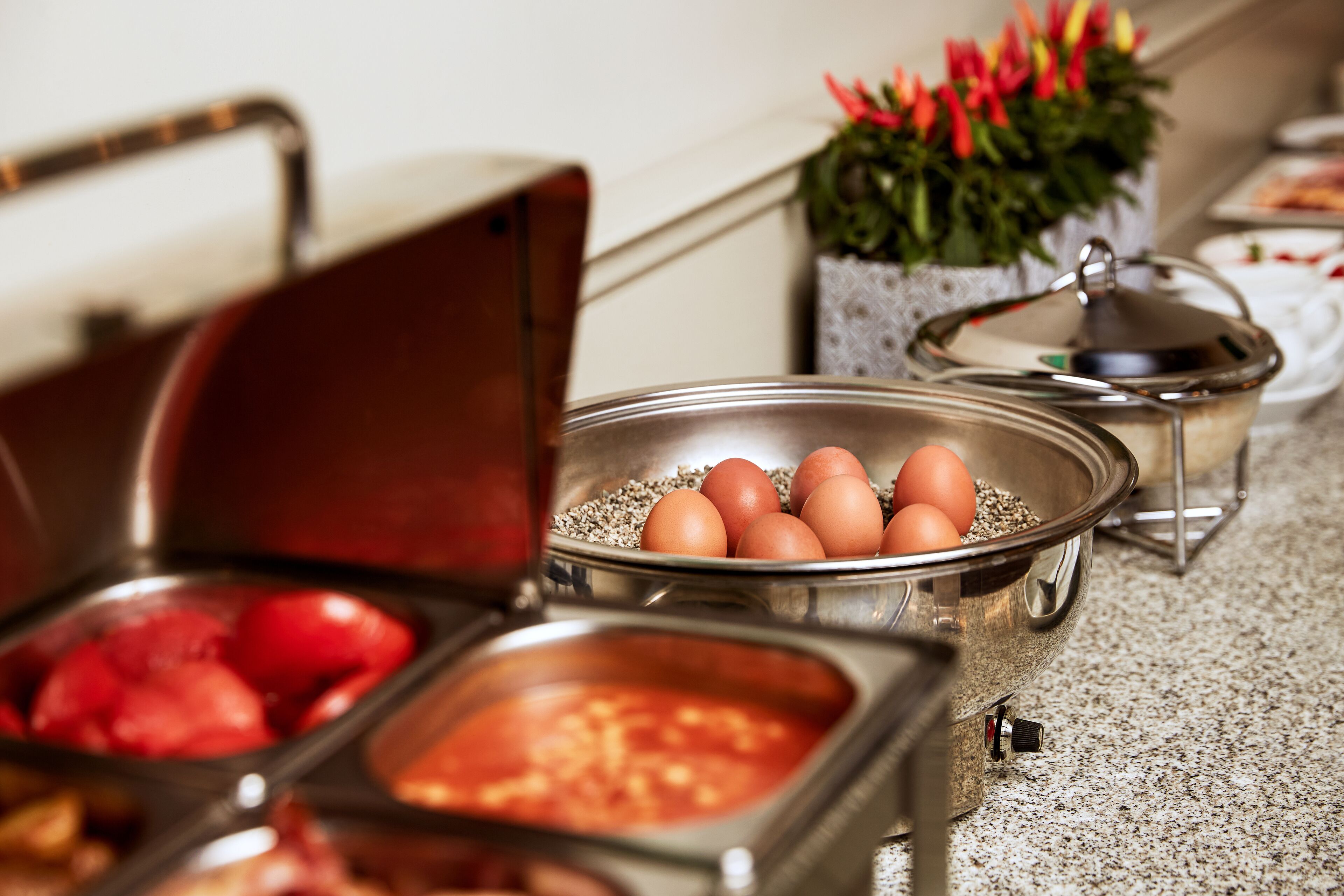 A buffet setup with various food items in metal containers, including eggs and what appears to be a red fruit dish.