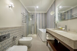 A modern bathroom with a shower, bathtub, and bidet. It features striped wallpaper, a granite countertop, and a large mirror.