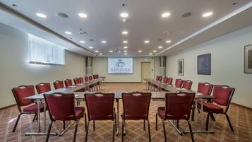 A conference room with a long table, red chairs, and a projector screen displaying the logo of Ratonda Central Hotels.