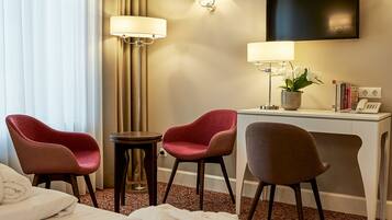 A hotel room with a bed, two chairs, a desk, a lamp, a TV, and a telephone.