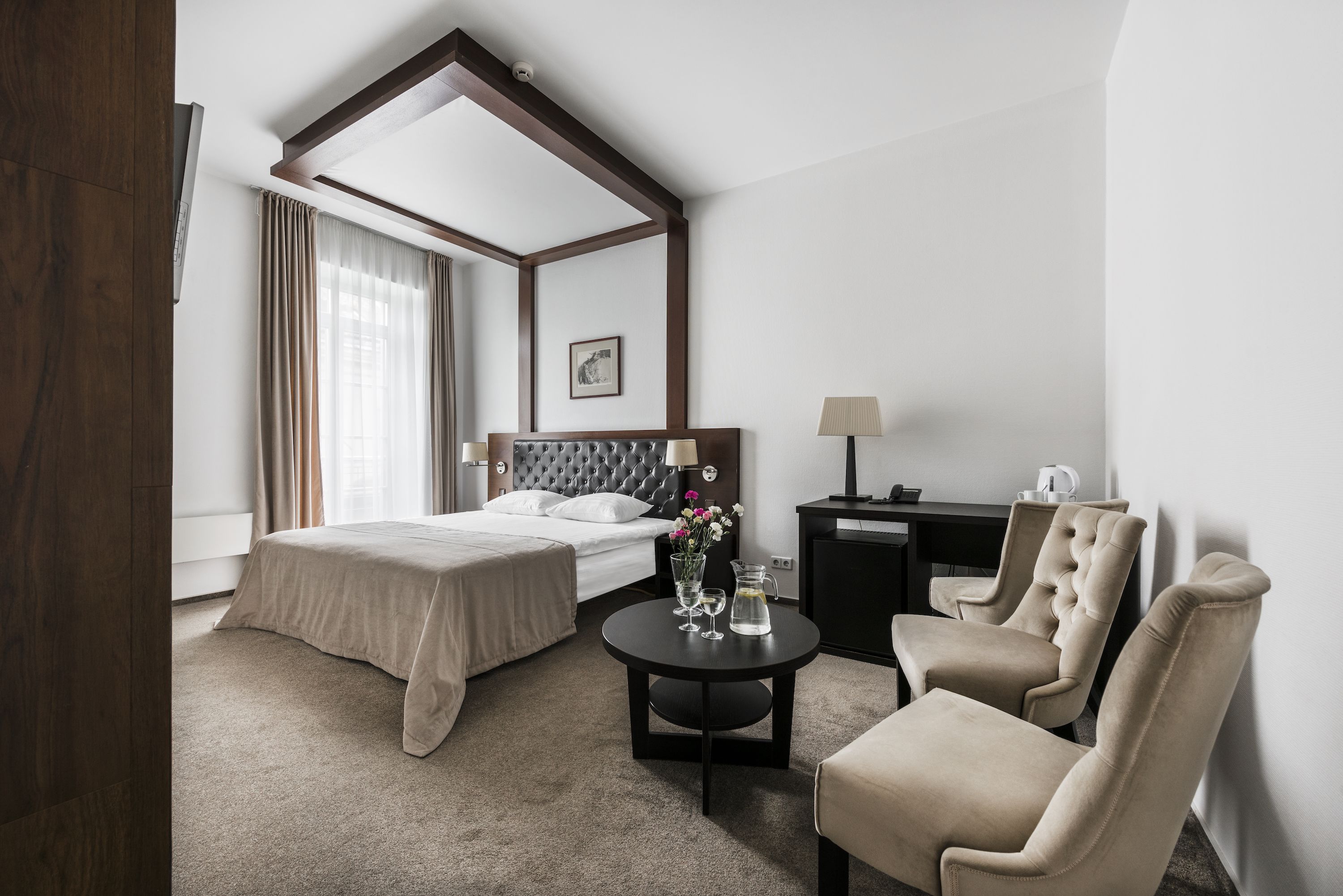 Een hotelkamer met een groot bed, een bureau, een stoel en een bijzettafeltje met een vaas en glazen.